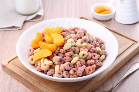 Téléchargez les photos : Bol plein de céréales fraîches avec du lait et des fruits à l'orange sur la table blanche - en image libre de droit