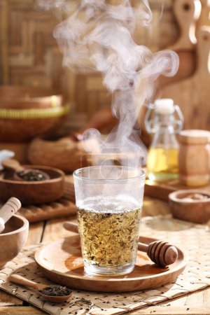 Foto de Té caliente en una taza de vidrio sobre una mesa con una cuchara de madera y un vaso de té - Imagen libre de derechos