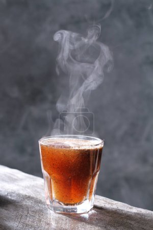 Téléchargez les photos : Un verre de thé chaud avec une cuillère sur fond noir - en image libre de droit