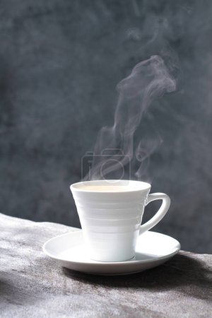Téléchargez les photos : Tasse blanche de café chaud sur un fond gris. le café du matin. tasse blanche avec une vapeur sur un fond sombre. - en image libre de droit