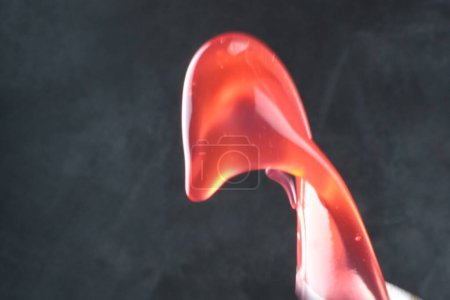 Téléchargez les photos : Liquide rouge dans le verre avec une goutte sur un fond noir - en image libre de droit
