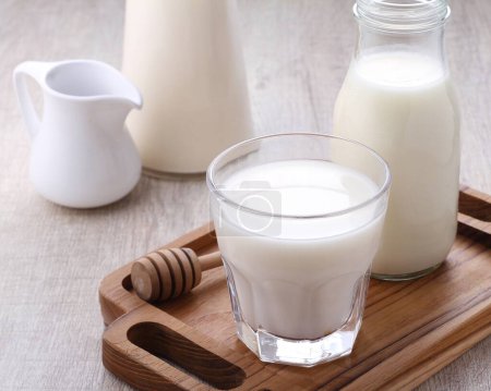 Téléchargez les photos : Verre de lait et de lait frais dans un plateau en bois avec une cruche et une paille. - en image libre de droit