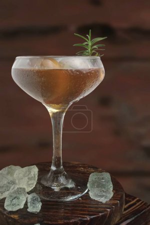 Téléchargez les photos : Un verre de cocktail avec un citron et une tranche de romarin sur un fond sombre - en image libre de droit