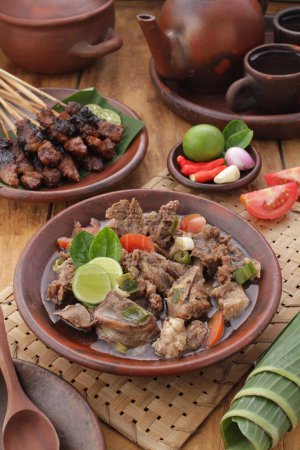 Téléchargez les photos : Nourriture indonésienne, soupe de chèvre servie avec jus de citron vert, tomates tranchées, oignons de printemps tranchés et sauce chili piquante - en image libre de droit