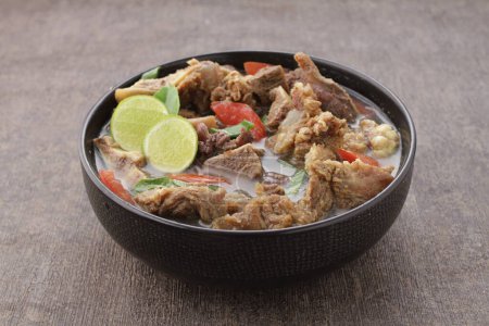 Téléchargez les photos : Nourriture indonésienne, soupe de chèvre servie avec jus de citron vert, tomates tranchées, oignons de printemps tranchés et sauce chili piquante - en image libre de droit
