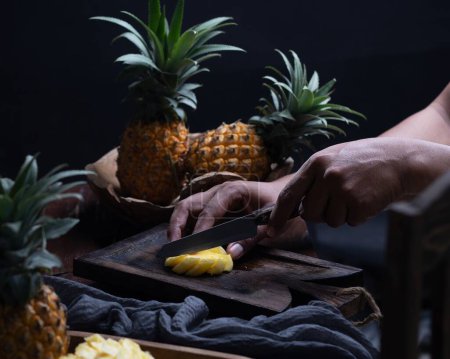 Téléchargez les photos : Plan rapproché d'une main tenant un ananas sur une table en bois - en image libre de droit