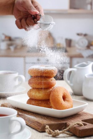 Photo for A person sprinkling sugar on a pile of donuts - Royalty Free Image