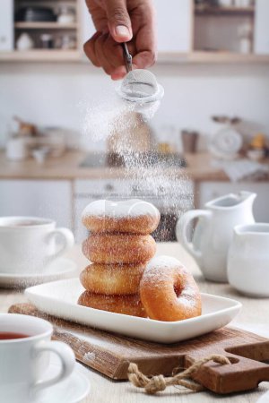 Photo for A person sprinkling sugar on a stack of doughnuts - Royalty Free Image