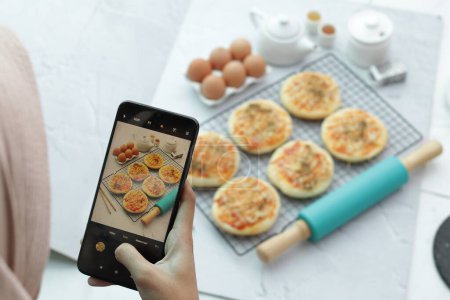 Photo for Woman taking picture of tasty macaroons with mobile phone in kitchen - Royalty Free Image