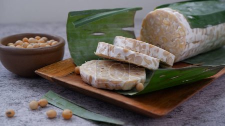 Tempeh crudo o tempe mentah. Rebanadas de tempeh en plato de madera. Semillas de soja crudas en un tazón de cerámica marrón. Tempe es producto de soja fermentada Originario de Indonesia.