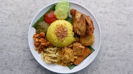 Téléchargez les photos : Nasi Kuning ou riz jaune sur une assiette blanche. Riz jaune au poulet frit traditionnel, au tofu, au tempeh et à la pomme de terre cassée. Indonésie nourriture. - en image libre de droit