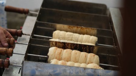 Téléchargez les photos : Kurtosh est fabriqué à partir de pâte à levure, dont une bande est filée, puis enroulée autour d'une broche de cuisson tronquée en forme de cône, et roulée dans du sucre granulé. Il est rôti au charbon de bois. Alimentation hongroise. - en image libre de droit