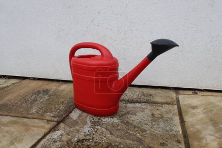 Photo for Red watering can on stone tiles with white wall background, a picture for eco gardener who works in the garden to help bloom plants and spray water on vegetation as a lifestyle or hobby in the summer - Royalty Free Image