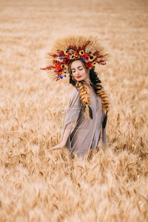 Hermosa joven ucraniana de pie sola en un campo de trigo amarillo. La morena mira a la cámara abrazando las espiguillas de trigo. Pacífico feliz Ucrania.