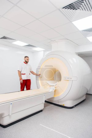 Foto de Un médico realiza una resonancia magnética o una tomografía computarizada de un paciente en una clínica moderna. Imágenes por resonancia magnética en el estudio del cuerpo humano. El médico prepara el aparato para la tomografía computarizada - Imagen libre de derechos