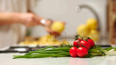 Foto de Close up view of woman in white shirt peeling a potato. Peel falling onto cutting board. Lady preparing potatoes to be cut and added to stock pot for dinner. - Imagen libre de derechos