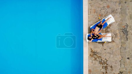 Téléchargez les photos : Un couple amoureux, un homme et une jeune femme, s'allongent sur des chaises longues près de la piscine, profitent de vacances tropicales et de la compagnie l'un de l'autre. Vue d'en haut. - en image libre de droit