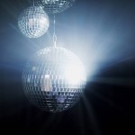 A colorful disco mirror balls illuminates the backdrop of a nightclub. The party lights up the disco ball.