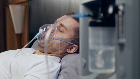 Téléchargez les photos : Portrait d'un jeune homme malade qui utilise un concentrateur d'oxygène et un inhalateur pour le traitement à la maison. covide-19, asthme bronchique. Traitement, traitement et procédures, thérapie. - en image libre de droit