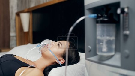 Foto de Retrato de una joven enferma que usa un concentrador de oxígeno y un inhalador para el tratamiento en casa. covid-19, asma bronquial. Tratamiento, tratamiento y procedimientos, terapia. - Imagen libre de derechos