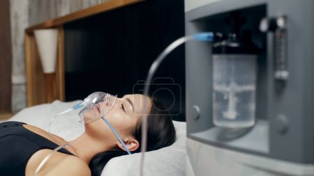 Photo for Portrait of a sick young woman who uses an oxygen concentrator and an inhaler for treatment at home. covid-19, bronchial asthma. Treatment, treatment and procedures, therapy. - Royalty Free Image