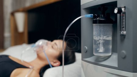 Téléchargez les photos : Portrait d'une jeune femme malade qui utilise un concentrateur d'oxygène et un inhalateur pour le traitement à la maison. covide-19, asthme bronchique. Traitement, traitement et procédures, thérapie. - en image libre de droit