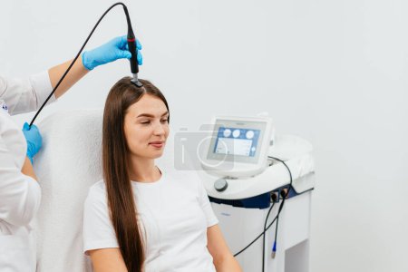 Photo for The cosmetologist makes the Microcurrent therapy against hair loss on the hair. Woman is doing a procedure to improve hair and scalp growth. Hair treatment in cosmetology using new technologies - Royalty Free Image