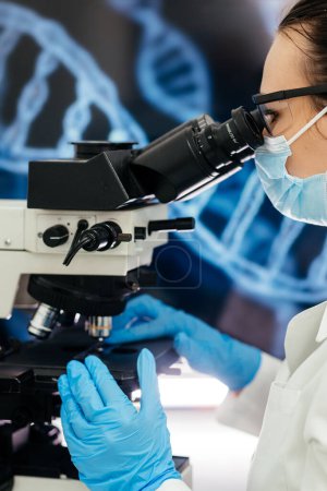 Foto de En un laboratorio médico moderno: un microbiólogo en gafas mira bajo un microscopio, analizando una muestra. Científico trabajando con equipos de alta tecnología. Primer plano - Imagen libre de derechos