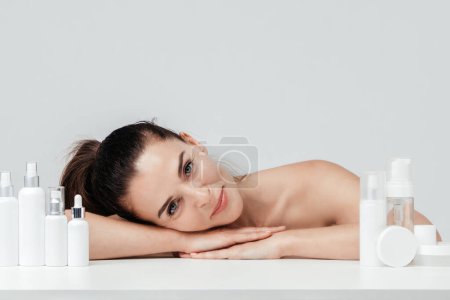 Photo for Mature Woman showing cosmetic products branding mockup. Daily skincare and body care routine. Natural cosmetic cream, serum, white bottles packaging, bio organic product. - Royalty Free Image