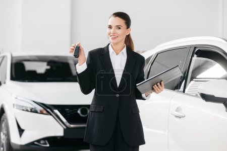 Photo for Beautiful business woman manager against the background of modern cars in the showroom of a car showroom. The concept of selling cars to customers, renting and complete equipment. - Royalty Free Image