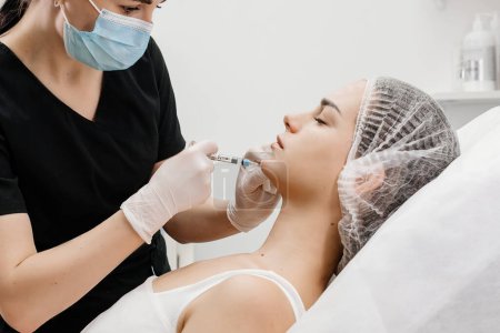 Ein Kosmetiker mit medizinischen Handschuhen führt einen kosmetischen Eingriff durch, um das Kinn zu vergrößern und das Gesicht zu korrigieren.
