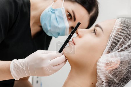 A cosmetologist wearing medical gloves performs a cosmetic procedure to enlarge the chin and correct the face.