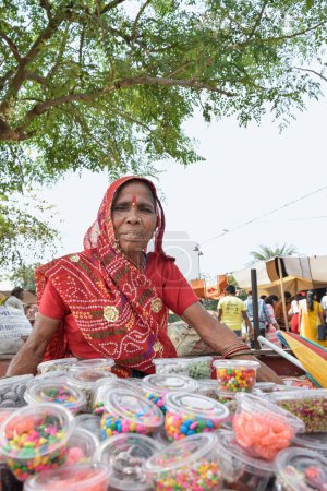 Ältere Frau im roten Sari verkauft Lebensmittel und Süßigkeiten auf dem Straßenmarkt in Jaipur, Indien.