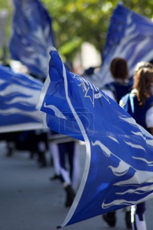 Photo for Team of spectacular blue dressed flag wavers with flags inflated by the wind walk in a street event - Royalty Free Image