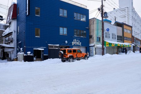 Téléchargez les photos : Hokkaido, Japan  - December 19, 2022 : A stylish orange Jeep is parked on the snow-covered street in Hokkaido - en image libre de droit