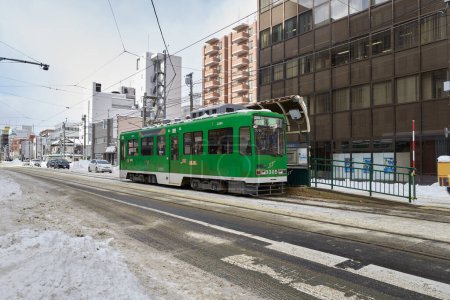 Photo for Hokkaido, Japan  - December 20, 2022 : Green tram on the snowy street of Sapporo City - Royalty Free Image