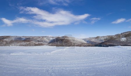 Photo for Snow fields with tire tracks and beautiful landscape with hills, blue sky and white clouds - Royalty Free Image