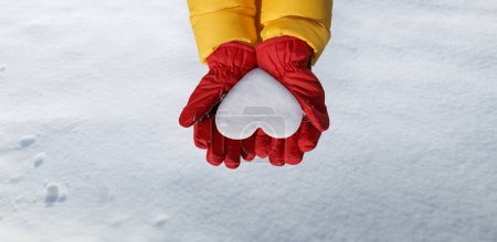 Téléchargez les photos : Panoramic view of hand in red glove holds snow heart on snow background. Romantic winter lovers concept - en image libre de droit