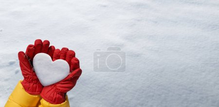 Foto de Panoramic view of hand in red glove holds snow heart on snow background. Romantic winter lovers concept - Imagen libre de derechos