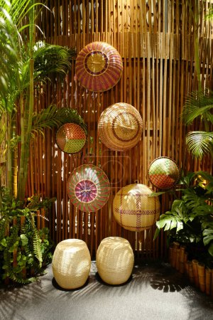 Foto de Expositor artístico de cestas hechas a mano contra una pared de bambú, rodeado de exuberante follaje - Imagen libre de derechos