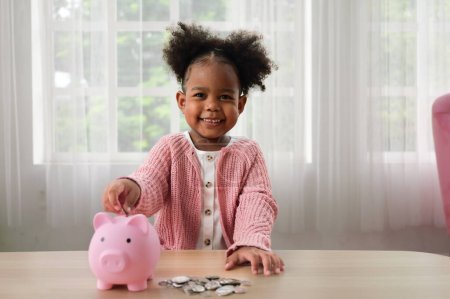 Téléchargez les photos : Petite fille mettant pièce de monnaie dans la tirelire en céramique, fille heureuse économiser de l'argent pour l'avenir dans la tirelire - en image libre de droit