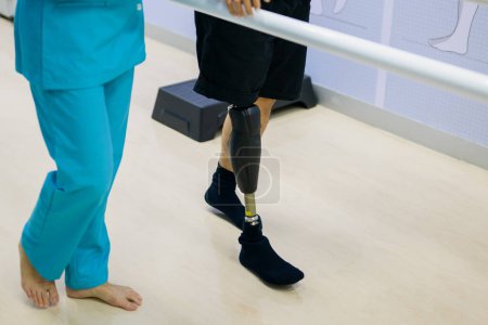 Photo for Physiotherapist helping patient with prosthetic leg walk between parallel bars during physiotherapy session at hospital, New artificial limb production for disabled people - Royalty Free Image