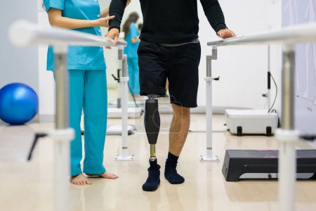 Photo for Physiotherapist helping patient with prosthetic leg walk between parallel bars during physiotherapy session at hospital, New artificial limb production for disabled people - Royalty Free Image