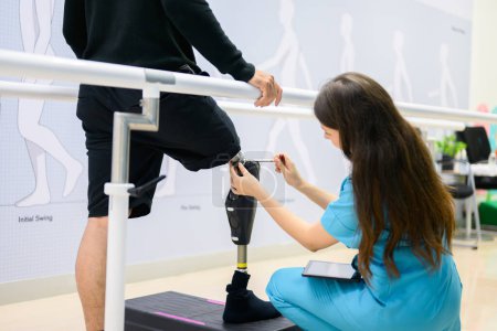 Téléchargez les photos : Physiothérapeute féminine ajustant la jambe prothétique du patient à l'hôpital, Patient handicapé avec traitement au centre de soins de santé, Nouvelle production de membres artificiels pour les personnes handicapées - en image libre de droit