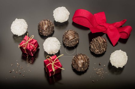 Foto de Variación de pralinés de chocolate con avellanas y bolas de coco para el día de Navidad con cinta atada roja. Dos pequeñas cajas cuadradas de Navidad. Decoración festiva. - Imagen libre de derechos