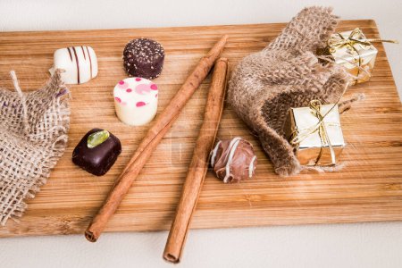 Foto de Mini pralinés de chocolate decorados con varilla de canela y pequeños paquetes en color oro dispuestos en la mesa. - Imagen libre de derechos