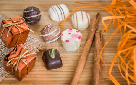 Foto de Pralinés de chocolate con decoración de paquete pequeño en color naranja y con palo de canela. - Imagen libre de derechos