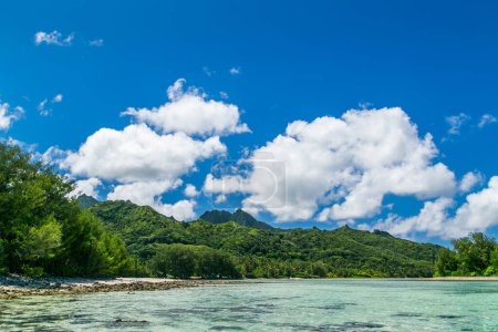 Tropische Bucht, paradiesische Destination auf den Cook Islands. Tropical Island Rarotonga, Küste mit Korallen. Azurblauer Himmel mit Wolken und türkisfarbenem Wasser an sonnigen Tagen. Leicht bewölkt. Blaues Meer mit kristallklarem Wasser. Hügel im Hintergrund.
