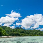 Tropical bay, paradise destination on the Cook Islands. Tropical Island Rarotonga, coast with corals. Azure blue sky with clouds and turquoise water during sunny day. Partly cloudy. Blue sea with crystal clear water. Hills in the background.