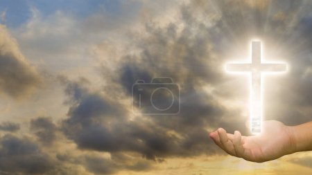 Image conceptuelle d'une croix chrétienne sur une main humaine sur un fond de ciel couchant